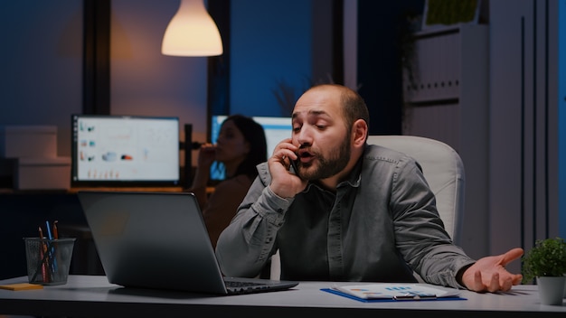 Stressed angry businessman sitting at desk table discussing corporate problem