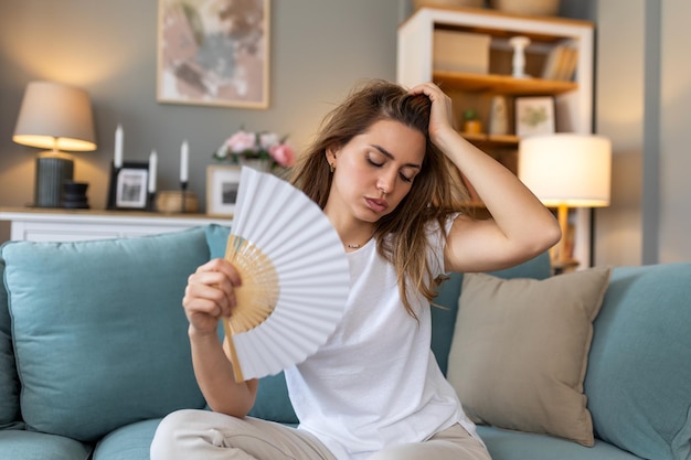 Stressed annoyed woman using waving fan suffer from overheating summer heat health hormone problem woman sweat feel uncomfortable hot in summer weather problem without air conditioner