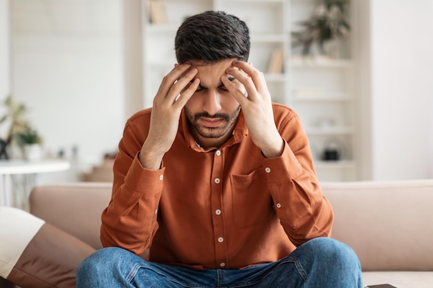 Stressed arab man sitting on couch and thinking