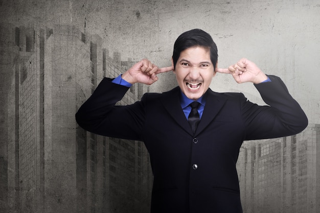 Stressed asian business man plugging his ears with fingers 