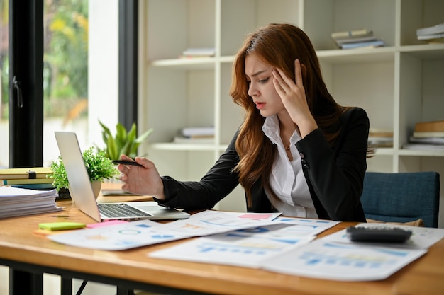 A stressed Asian businesswoman focuses on working on her business financial reports