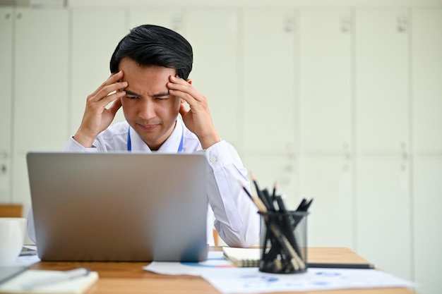 Stressed Asian male office worker having trouble with the financial data on his computer