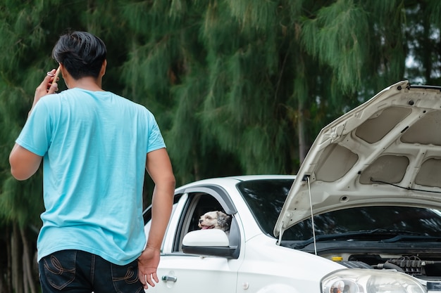 Stressed asian man using mobile phone while the car broken down with his lovely dog