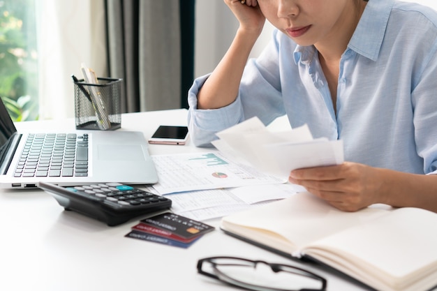 Stressed asian woman checking bills, taxes, bank account
balance and calculating credit card expenses. family finance, debt
management concept. close up