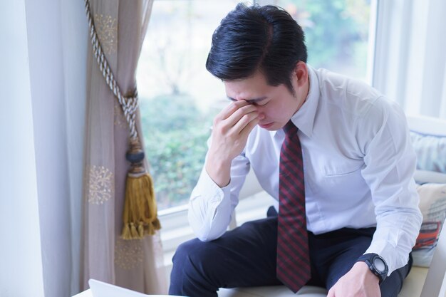 Giovane testa asiatica sollecitata della tenuta dell'uomo d'affari con le mani che guardano giù. emozioni umane negative espressione facciale sentimenti.