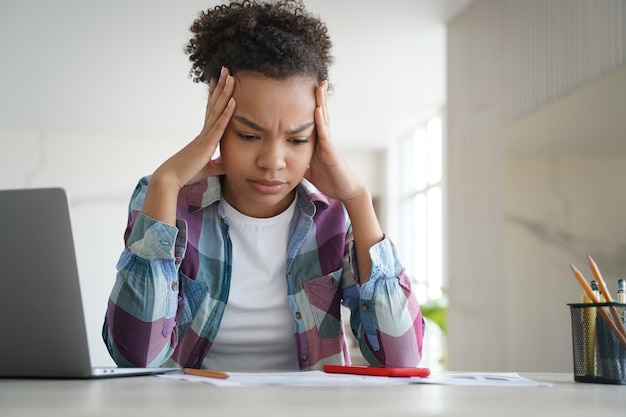 Stressed biracial teen girl school student doing homework at laptop Difficult elearning stress