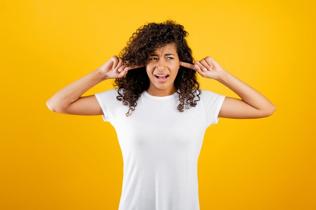 Stressed black girl covering her ears isolated over yellow