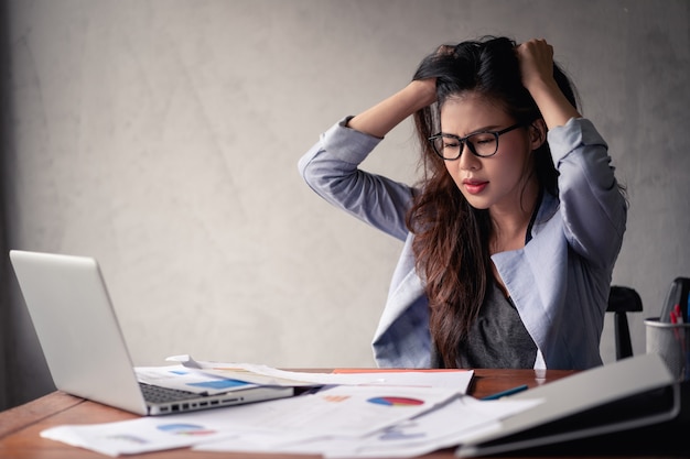 Foto donna asiatica sollecitata di affari che per mezzo del computer portatile e di lavoro