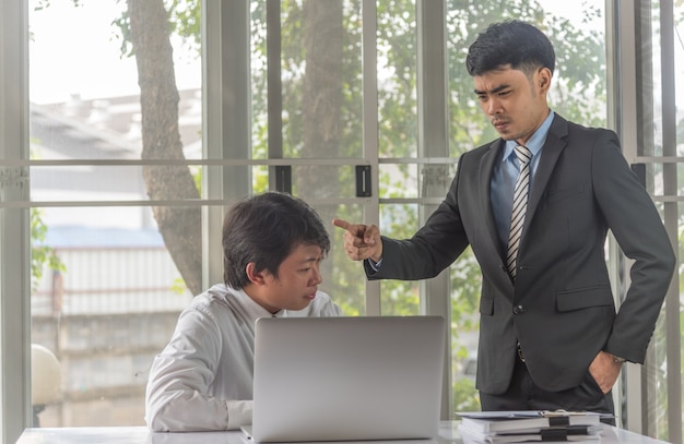 Uomo sollecitato di affari che lavora con il computer portatile sullo scrittorio che si lamenta sporgenza del capo arrabbiato dell'uomo