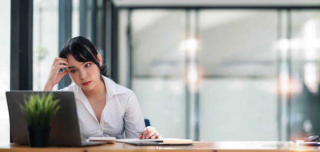 Stressed business woman working at office on laptop and document looking worried tired and overwhelmed