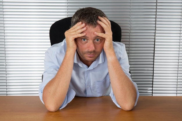 Stressed businessman sitting at desk holding his head and worrying