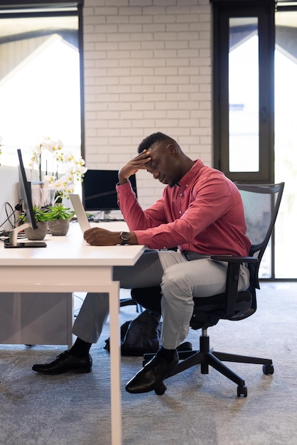 Stressed businessman sitting at desk looking at tablet in modern office