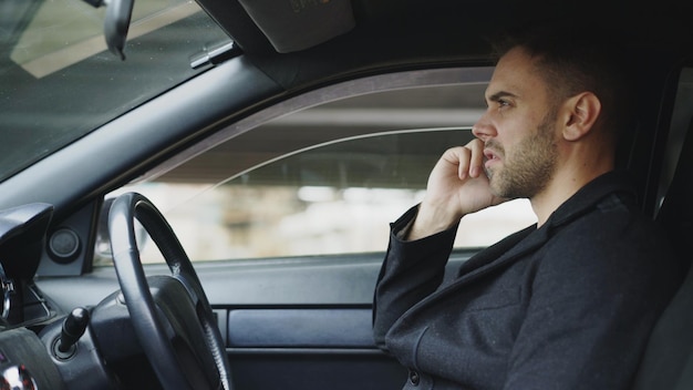 屋外の車の中に座っている間、ビジネスマンが宣誓し、電話を話すことを強調しました