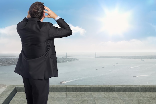 Stressed businessman with hands on head against coastline city