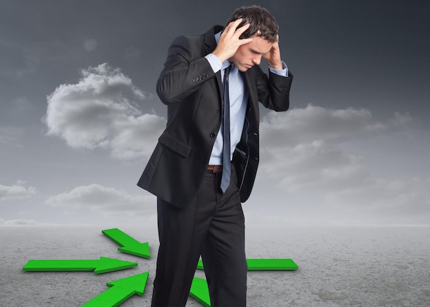 Photo stressed businessman with hands on head against green arrows in a desert landscape