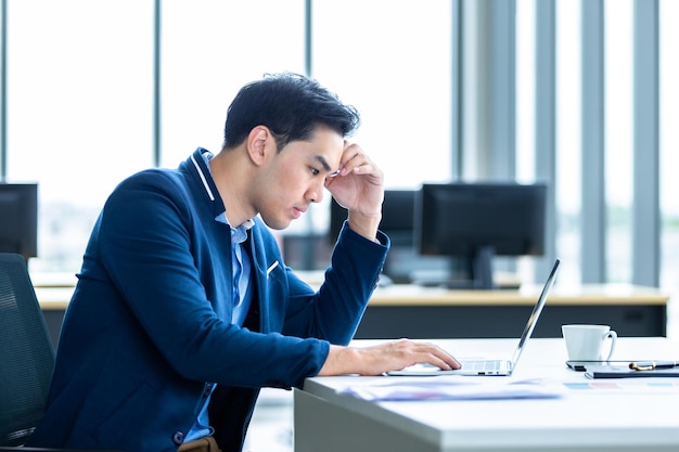 L'uomo d'affari stressato ha lavorato con un computer portatile e ha avuto un mal di testa dopo le perdite di affari sullo sfondo della stanza dell'ufficio