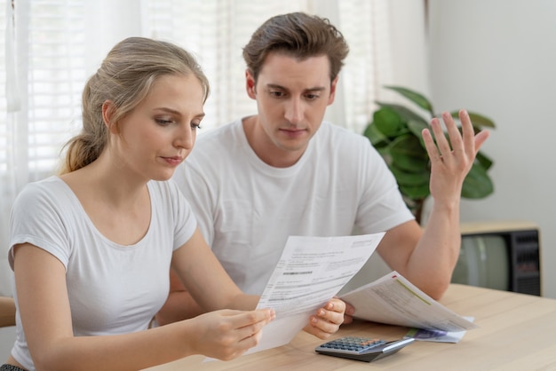 Stressed couple young family financial troubles sitting in\
living room at home and holding expenses bills from the bank, woman\
worried on money to pay a debt. financial problems concept.