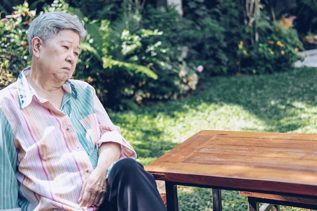 Stressed depressed fatigued sad upset asian old asian elderly senior elder woman sitting in garden.