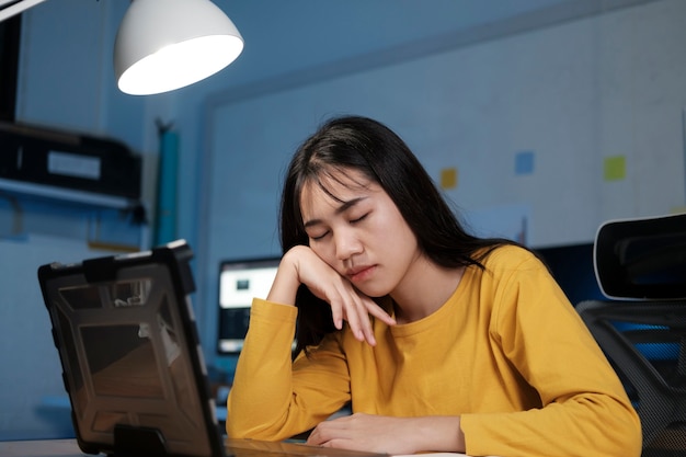 Stressed exhausted woman sitting at office desk and working overtime, she is overloaded with work.