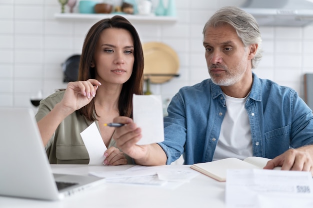 Stressed family couple feeling disappointed by high utility bills, money loss. Unhappy nervous married spouse received debt mortgage notification, checking financial documents.