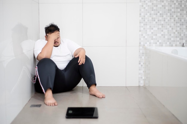 Stressed fat man sitting with a scale