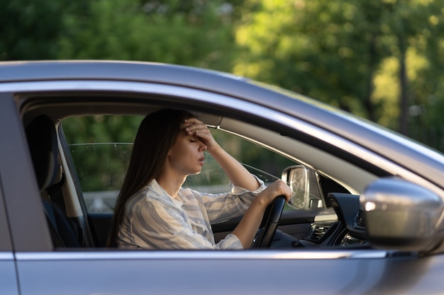 Ragazza stressata con mal di testa guida l'auto frustrata dispiaciuta giovane autista femminile soffre di malattia