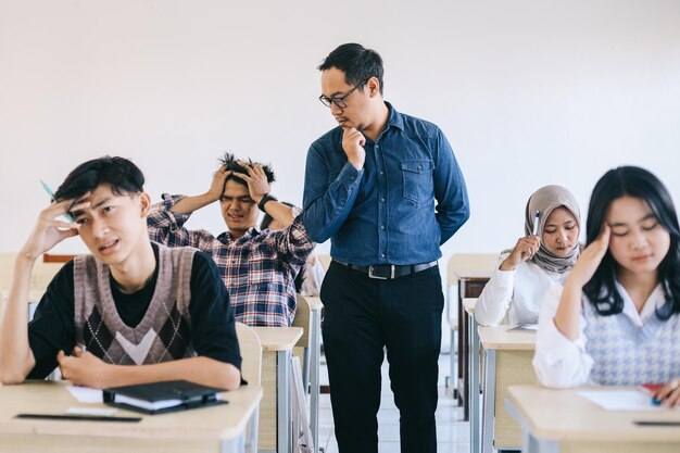 Stressed high school students having test at classroom while teacher is watching