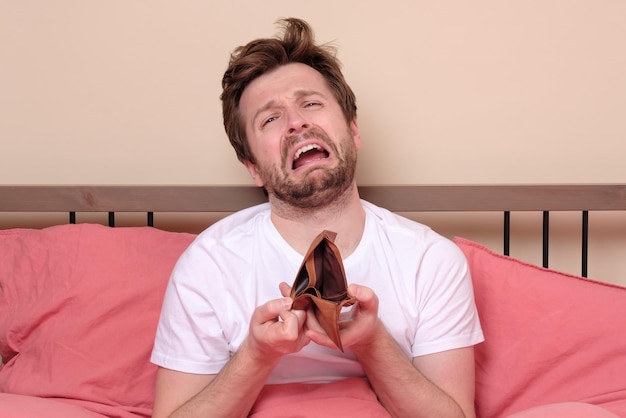 Stressed man being confused about his empty wallet sitting at bed in quarantine