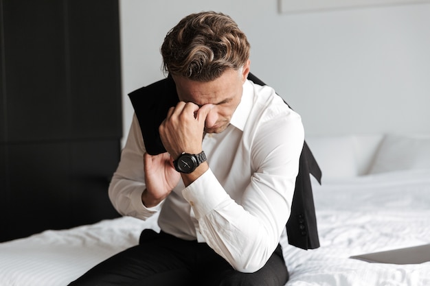 Stressed man dressed in suit sitting on bed