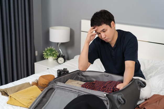 stressed man having problem with packing clothes into suitcase on bed holiday travel concept