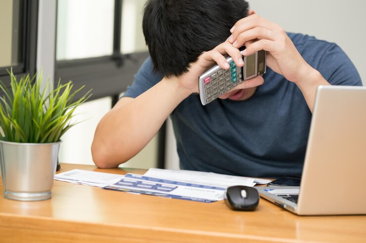 Photo テーブルに座っている間にラップトップの上に計算機を握っているストレス状態の男性