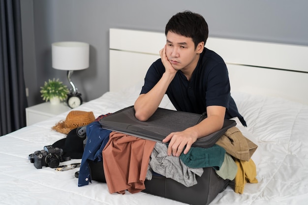 Stressed man trying to close overfilled suitcase on bed