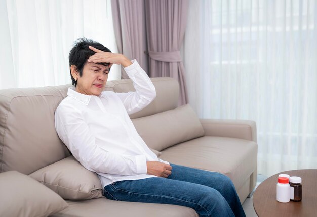 Photo stressed mature senior woman touching head with closed eyes at sofa in living room suffering from headache migraine blood pressure problem health problems feeling strong pain