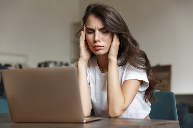 a stressed negative young woman with headache indoors at home using laptop computer.