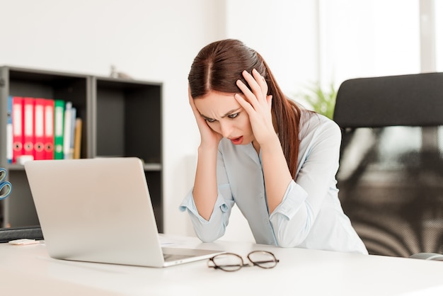 Stressed out woman behind laptop holding her head in the office