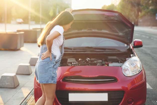 Stressed pregnant woman standing near broken car on city street