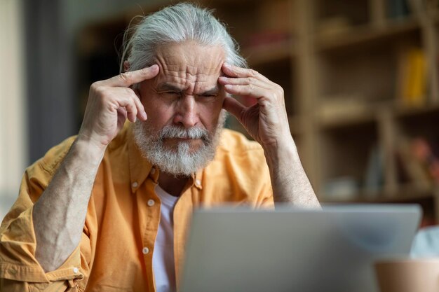 Uomo anziano stressato che lavora da casa utilizzando il computer portatile