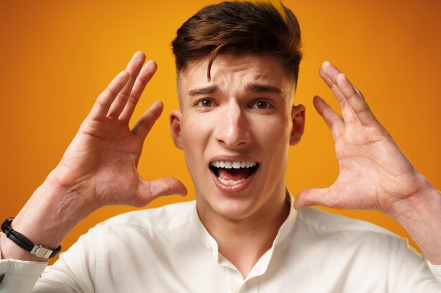 Stressed shouting young man holding hands near his head