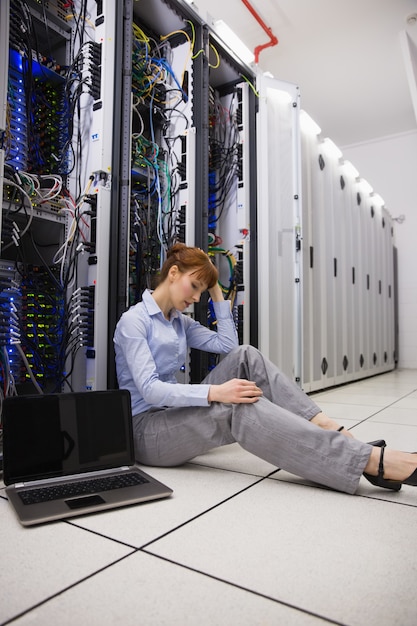 Stressed technician sitting on floor beside open server