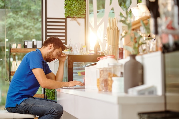 Stressed and tired coffeeshop owner analzying expenses when working on laptop at counter