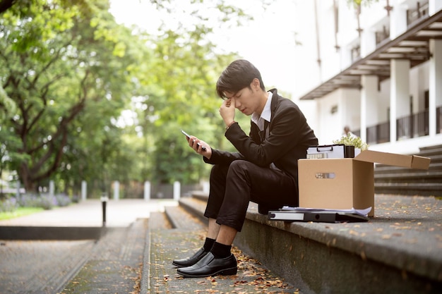 A stressed and upset Asian businessman sits on a staircase after getting fired or losing his job