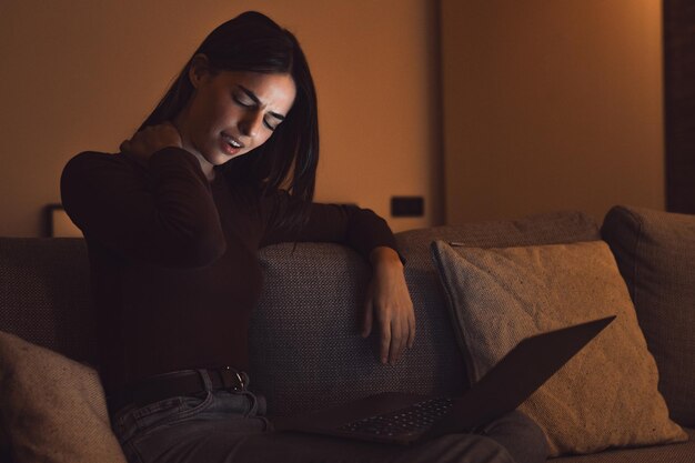 Stressed woman at late night having strong terrible neckache attack after computer laptop study sleepy exhausted girl suffering from chronic migraine massaging muscle to relieve neck ache tensionxA