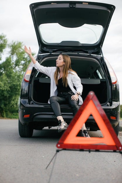 壊れた車を見て、側面図で田舎道でエンジンをチェックしているストレスの多い女性