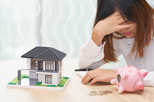 Photo stressed woman with running out of money in piggy bank and her house