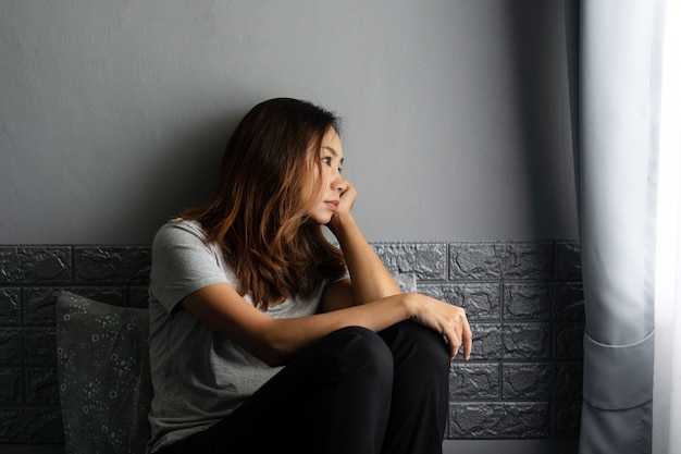 Stressed young Asian woman suffering on depression and sitting alone on bed in dark room at home