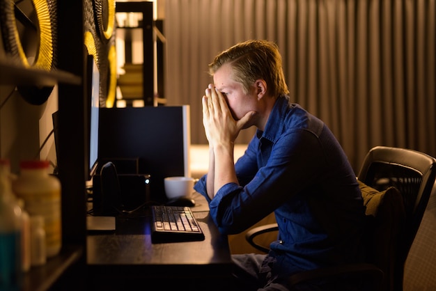 Stressed young businessman looking tired while working overtime at home late at night