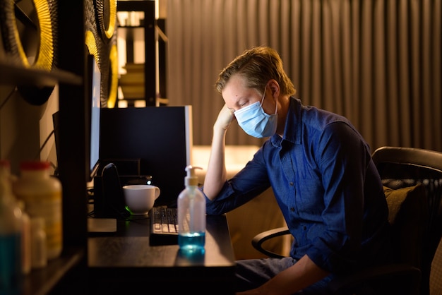 Stressed young businessman with mask looking tired while working from home late at night