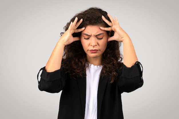 Stressed young businesswoman with pained face expression holding her head in frustration or headache