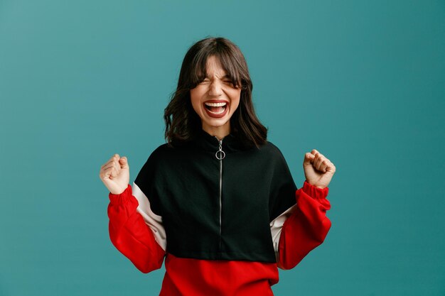 Stressed young caucasian woman keeping fists in air screaming with closed eyes isolated on blue background