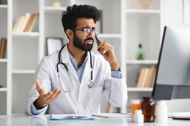 Stressed young eastern doctor have phone conversation clinic interior